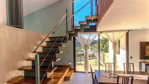 A modern interior with a staircase leading to a balcony, a dining area with chairs, and a view of greenery outside. - Stunning modern villa - just half hour to Barcelona! (Caldes De Montbui)