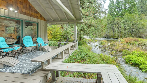 A wooden deck with outdoor seating and a view of a stream. - Fishing & Rafting: McKenzie River Cabin! (Mckenzie Bridge)
