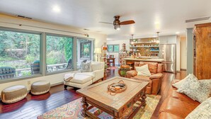 A spacious living room with a large window, a ceiling fan, and a kitchen area in the background. - Fishing & Rafting: McKenzie River Cabin! (Mckenzie Bridge)