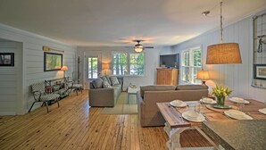 A spacious living room with a wooden floor, a sofa, a dining table set for four, and a television in the background. - Harrison Lakefront Cottage w/ Private Dock! (Harrison)