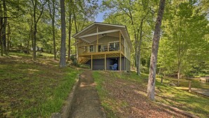 A wooden cabin with a balcony, surrounded by trees and a pathway leading to it. - Harrison Lakefront Cottage w/ Private Dock! (Harrison)