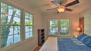 A bedroom with a large bed, a ceiling fan, and multiple windows offering views of a body of water. - Harrison Lakefront Cottage w/ Private Dock! (Harrison)