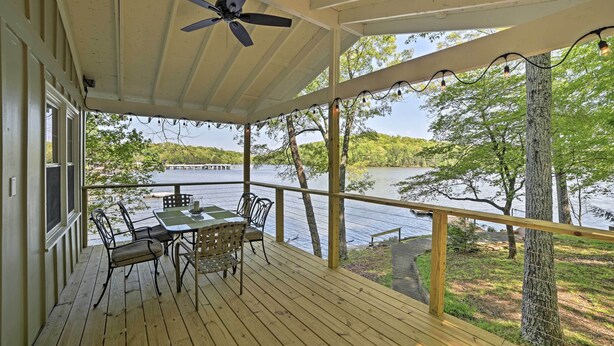 A wooden deck with a table and chairs, overlooking a lake with trees and a dock. - Harrison Lakefront Cottage w/ Private Dock! (Harrison)
