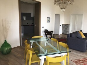 A dining area with a glass table and yellow chairs, a dark sofa with a yellow pillow, and a chandelier. - Casa del Cedro superior apartment with private garden on the Gulf of Naples. (Napoli)