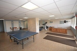 Una habitación amplia con mesa de ping pong, equipo de ejercicio y un banco de madera.