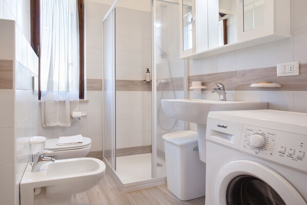 Ein modernes Badezimmer mit einer Duschkabine, einem Waschbecken, einer Toilette und einer Waschmaschine mit Frontlader.