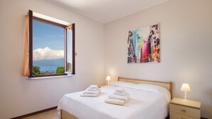 A bedroom with a bed, two bedside tables, a window with a view, and a painting on the wall. - Apartment Rosa Portland With Pool (Lazise)
