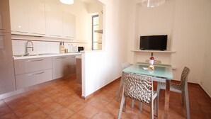 A modern kitchen with white cabinets, a built-in oven, and a dining area with a glass table and patterned chairs. - Walk to the Colosseum from your Family Apt (Roma)