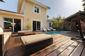 Une terrasse en bois avec des meubles d’extérieur, une piscine et un bâtiment doté de grandes fenêtres.