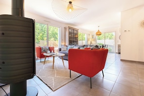 A spacious living area with a red chair, a round table, and a large window.