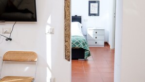 Un corridoio che porta a una camera da letto con televisione, una poltrona, un letto e un quadro appeso al muro.