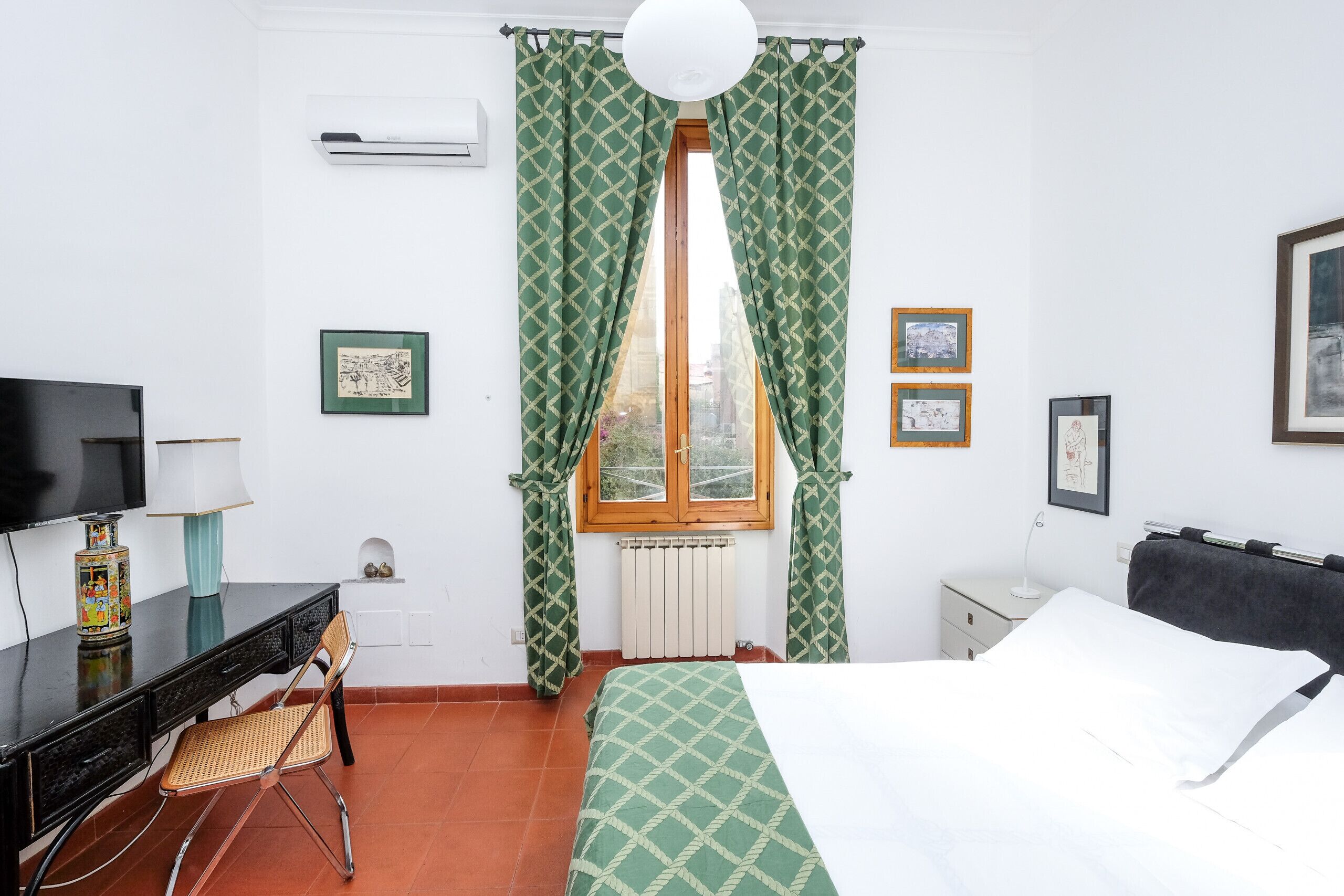 Une chambre d’hôtel avec un lit, un bureau doté d’une lampe, une chaise, un téléviseur et des tableaux encadrés au mur.