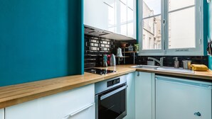A modern kitchen with white cabinets, a wooden countertop, and a window with a view of buildings.