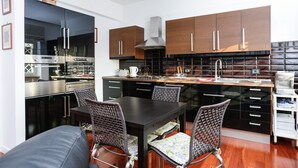 A modern kitchen with dark wooden cabinets, stainless steel appliances, and a dining area with wicker chairs. - Enjoy the Sunset on Your Vatican Terrace (Roma)