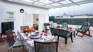 A covered outdoor patio with a table set for a meal, chairs, and a TV. - Enjoy the Sunset on Your Vatican Terrace (Roma)