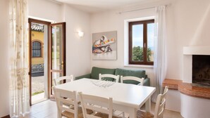 A dining area with a white table and chairs, a green sofa, a fireplace, and a painting on the wall. - Apartment Rosa Sweet Sara With Pool (Lazise)