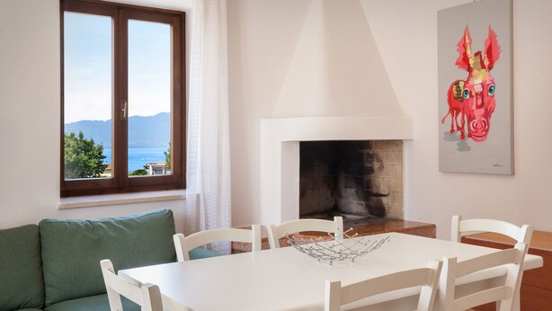 A dining area with a white table and chairs, a green sofa, a fireplace, and a painting on the wall. - Apartment Rosa Sweet Sara With Pool (Lazise)
