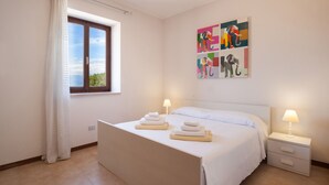 A hotel room with a bed, two bedside tables, a window with curtains, and a wall with abstract art. - Apartment Rosa Sweet Sara With Pool (Lazise)