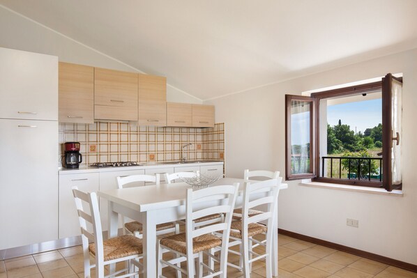 Une cuisine moderne avec des meubles blancs, une table à manger entourée de chaises blanches et une fenêtre donnant sur un paysage verdoyant.