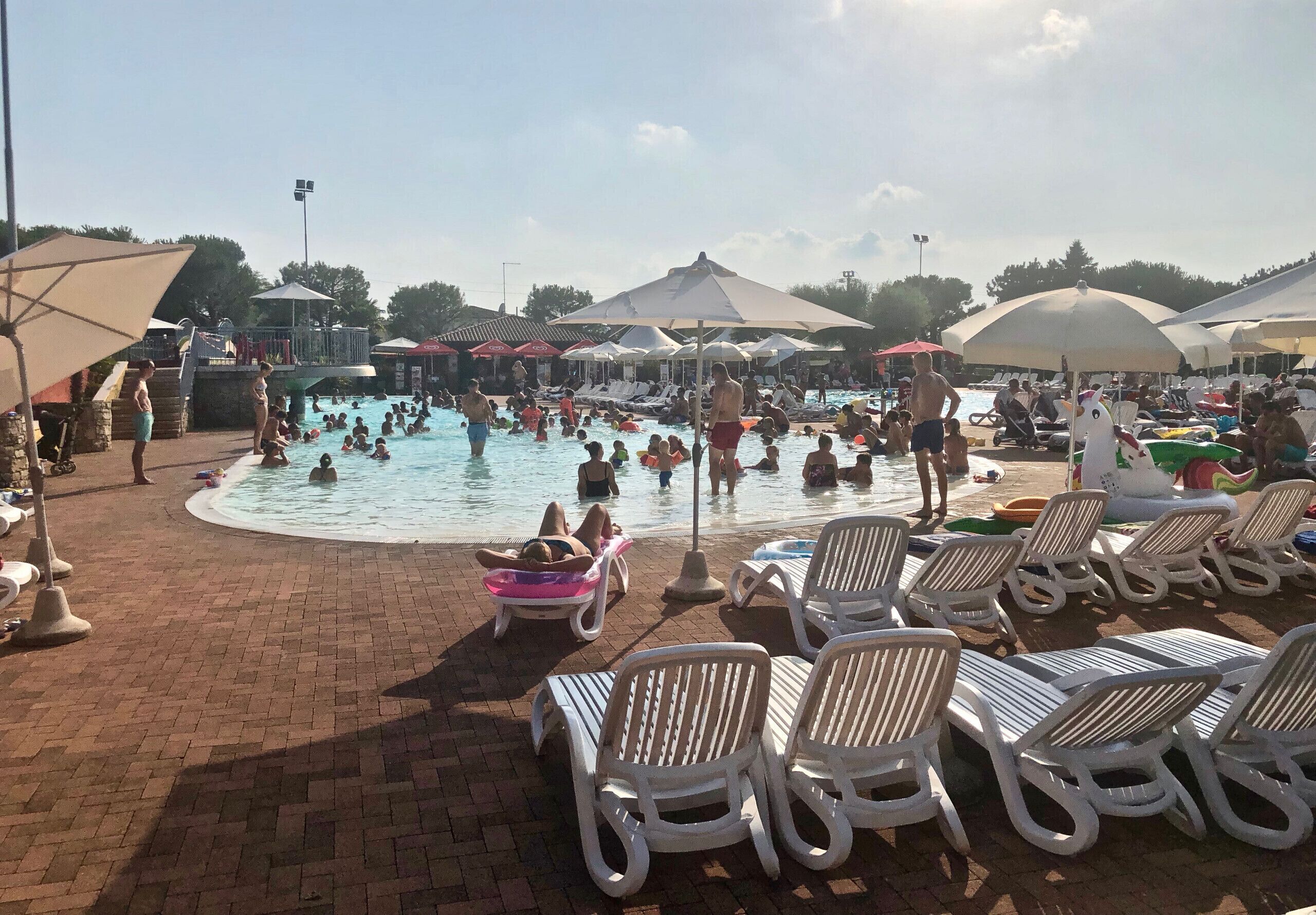 Un espace piscine doté de plusieurs chaises longues et de parasols, entouré d’un chemin pavé en briques.