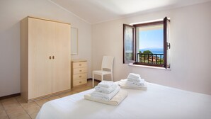 A bedroom with a large wardrobe, a chair, a bed with neatly folded towels, and a balcony with a view. - Apartment Rosa Noisette With Pool (Lazise)