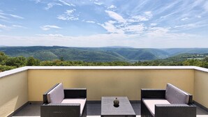 A balcony with two wicker chairs and a small table, overlooking a mountainous landscape.