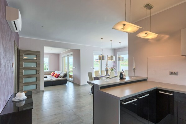 A modern kitchen with a central island, pendant lighting, and a view to a living area with a sofa and chairs. - Villa Karli (Sutivanac)