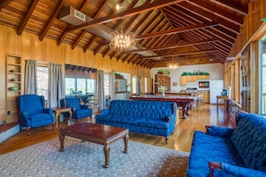 Un salón espacioso con vigas de madera, un sofá azul, una mesa de centro de madera y un comedor con mesa y sillas de madera.
