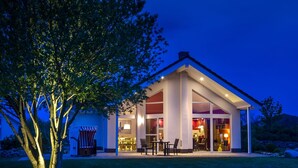 A modern house with a large glass front, a tree in the foreground, and a well-lit patio area. - located at the sea, stunning view over Hiddensee and the iconic lighthouse (Trent OT Vaschvitz)