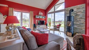 A cozy living room with a red wall, a fireplace, a television, and a large window. - located at the sea, stunning view over Hiddensee and the iconic lighthouse (Trent OT Vaschvitz)