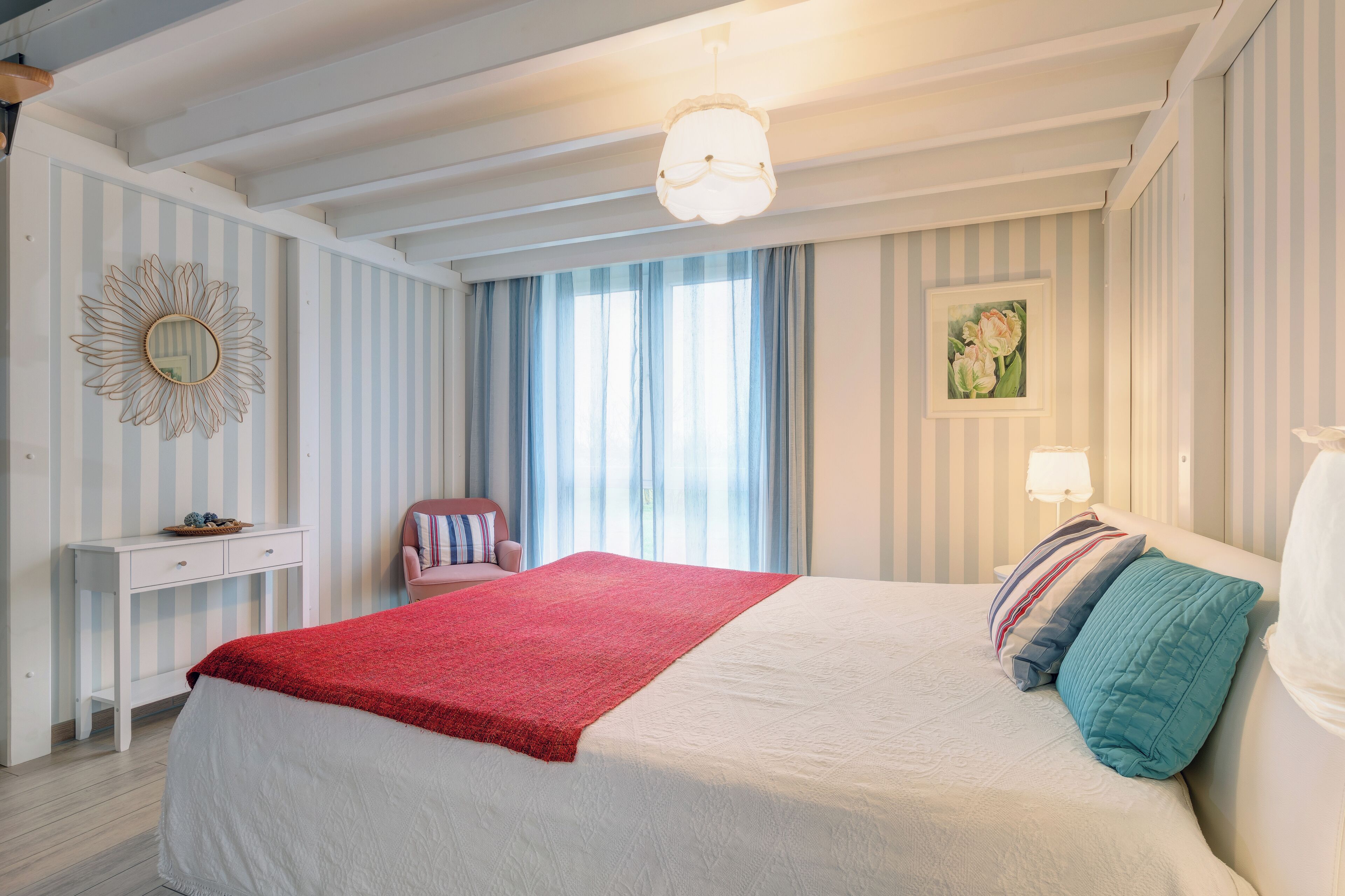 Un dormitorio con cama, mesita de noche, silla, ventana con cortinas, un reloj de pared y un cuadro.