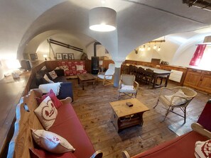 A cozy interior with a wooden floor, a red sofa, a wooden table, and a dining area with chairs and a table.