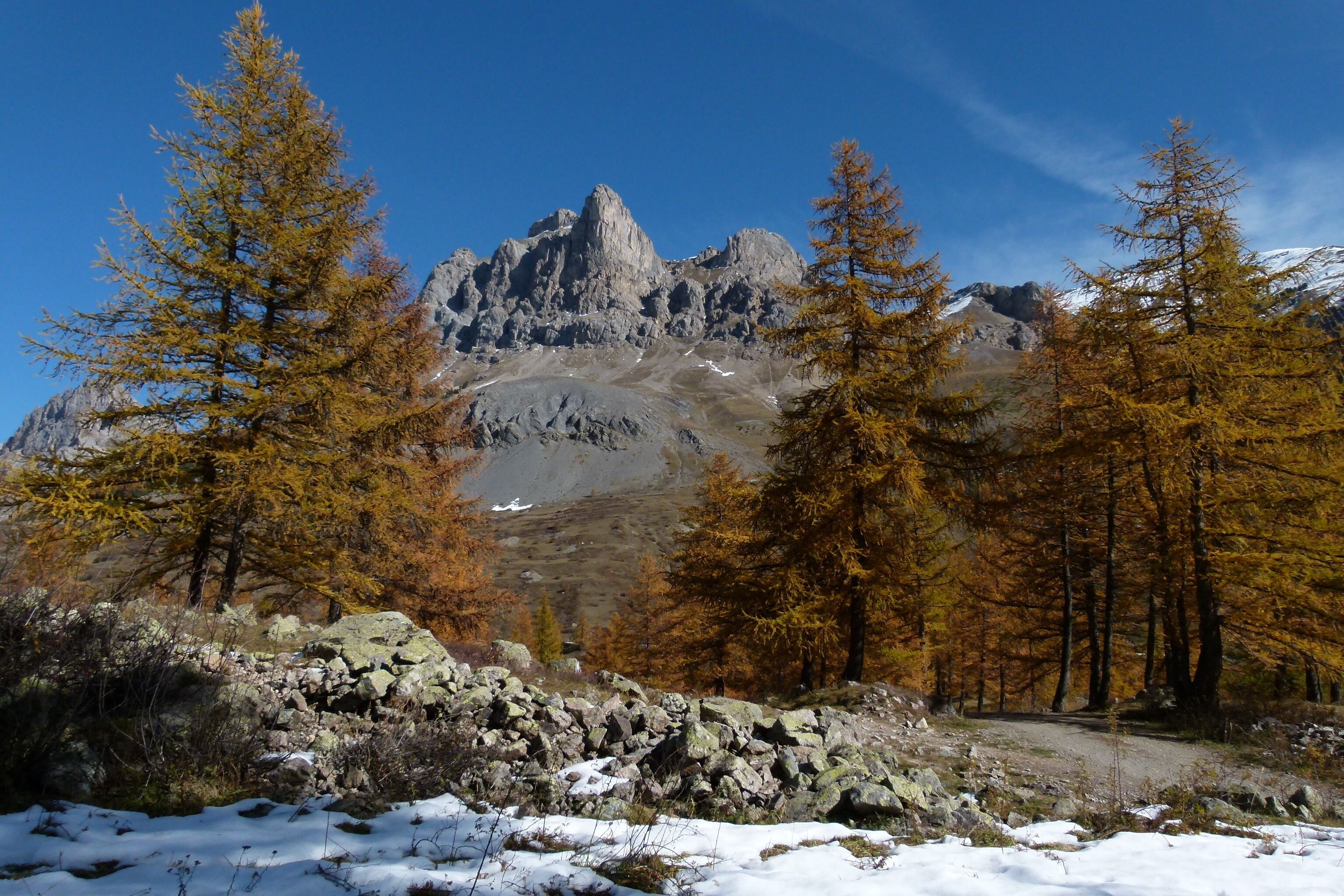 A mountainous landscape with rocky terrain, autumn-colored trees, and a clear sky.