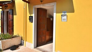 A yellow building with a wooden door, a mailbox, and a number sign indicating the address. - Apartment Rosa Bourbon With Pool (Lazise)