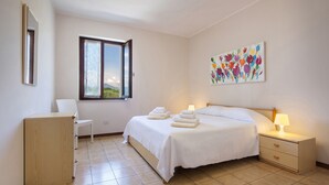 A bedroom with a bed, a nightstand, a chair, a cabinet, a window, and a painting on the wall. - Apartment Rosa Bourbon With Pool (Lazise)