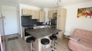 A modern kitchen with wooden cabinets, a central island with stools, a refrigerator, and a painting of a cat on the wall.