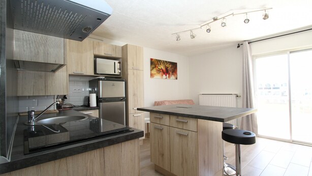 A modern kitchen with a sink, stove, and microwave. There is a window with a view of buildings outside.