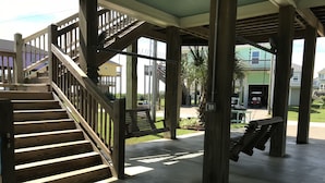 Un espacio al aire libre techado con escaleras de madera, una hamaca y piso de concreto.
