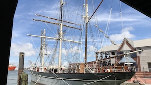 Un gran barco velero amarrado en un puerto deportivo, con un edificio al fondo.