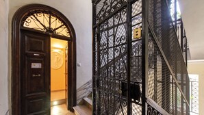Una puerta de madera oscura con un letrero, un portón de metal con un diseño decorativo y una escalera de mármol.