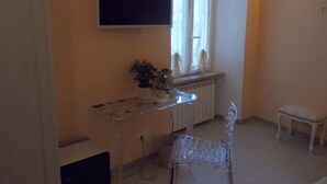 Una habitación con un televisor montado en la pared, una mesita con una planta, una silla y un radiador.