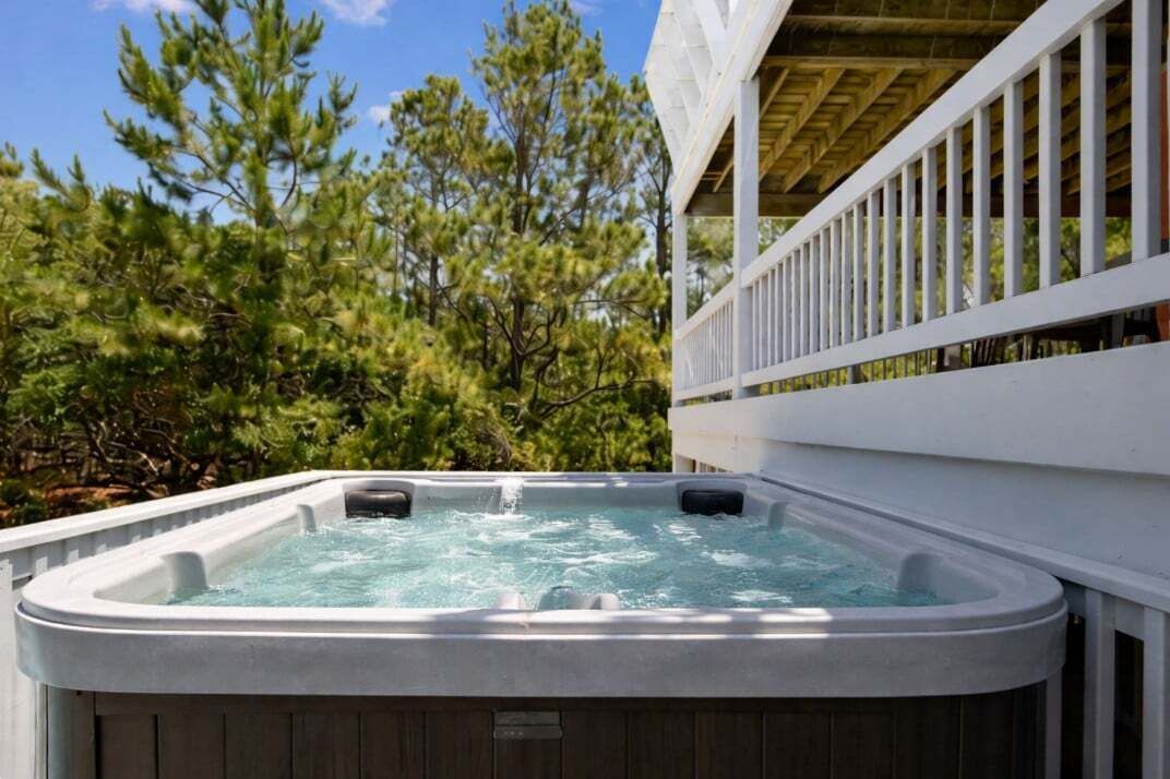 A hot tub with a wooden deck and white railings, surrounded by trees.