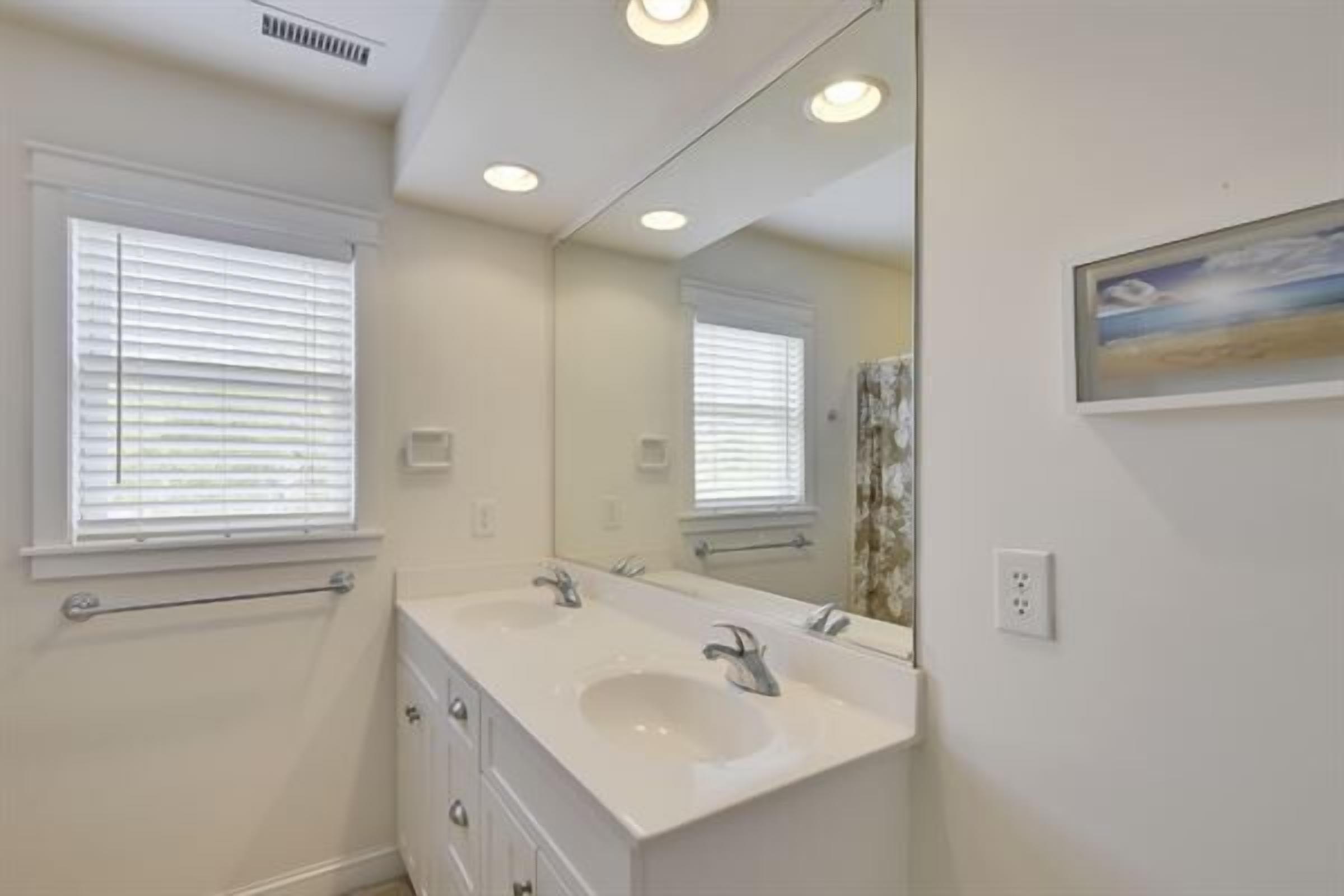 A bathroom with two sinks, a large mirror, and a window with blinds.