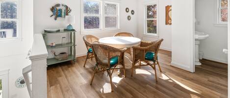 A dining area with a round table and wicker chairs, white walls, and wooden flooring.
