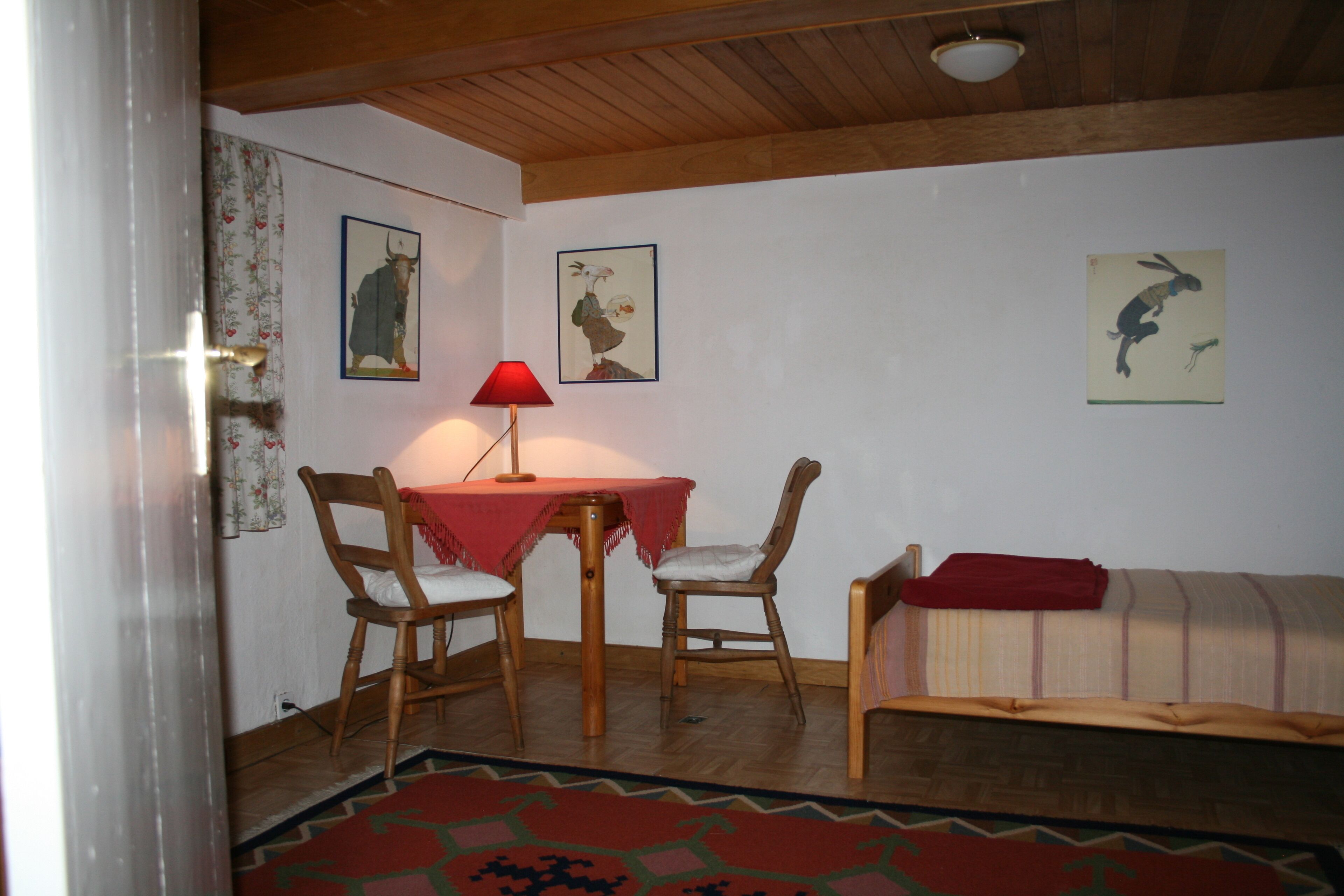 A cozy room with a wooden ceiling, a table with chairs, a sofa, and a patterned rug.
