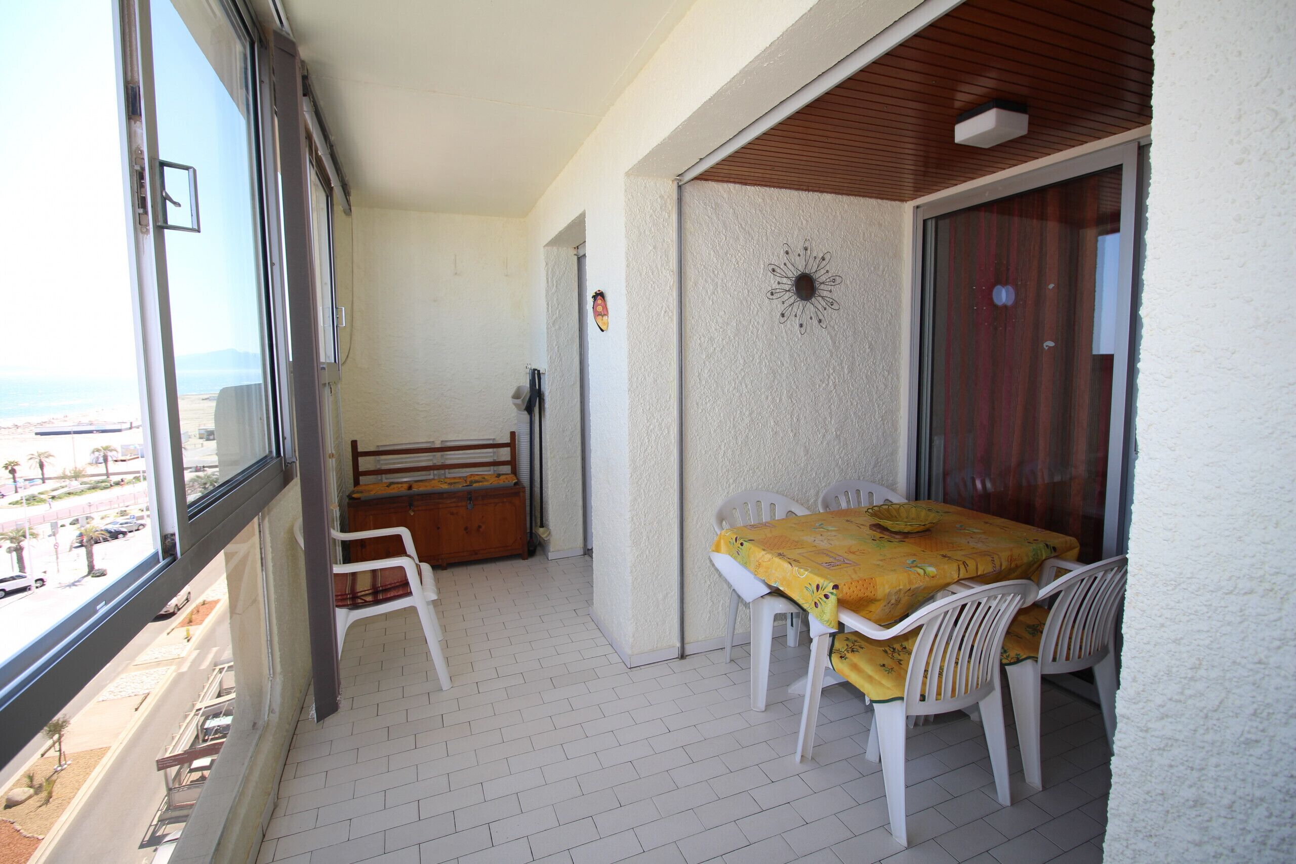 A balcony with a table and chairs, a wooden bench, and a view of the beach.