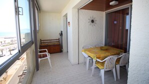 A balcony with a table and chairs, a wooden bench, and a view of the beach. - 2 room apartment with sea view and parking (Canet-en-Roussillon)