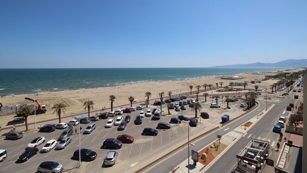 A parking lot with cars, a beach, and a road with palm trees. - 2 room apartment with sea view and parking (Canet-en-Roussillon)