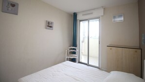 A bedroom with a bed, a chair, a wardrobe, and a sliding glass door leading to a balcony. - 2 room apartment with sea view and parking (Canet-en-Roussillon)
