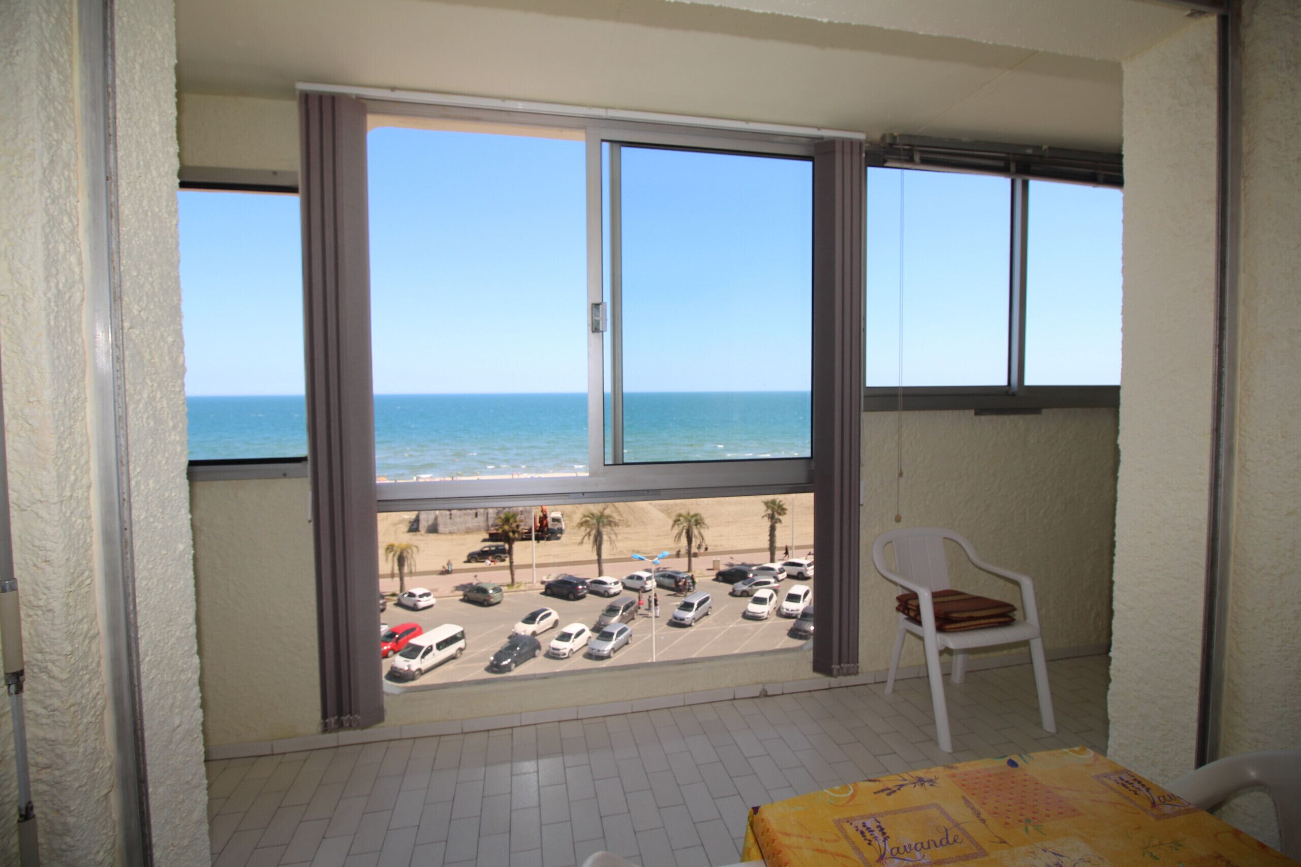A balcony with a view of the beach and parked cars.